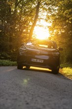 A car on a road surrounded by trees, soft sunlight behind the vehicle, electric car, VW ID5,