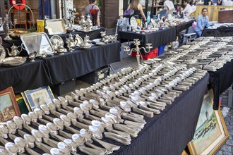 A flea market with numerous stalls displaying antique silver cutlery and other items, Paris