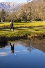 Male Golfer Reflected in a Water Pond and Hitting the Golf Ball on Fairway on Golf Course with