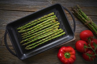 Asparagus grilled on cast iron grill pan on wood table with tomatoes and pepper