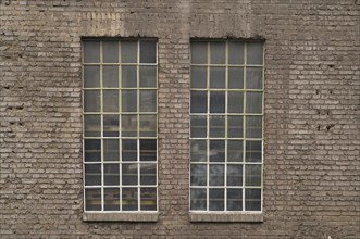 Two large industrial windows with small panes and metal frames are set in an old brick wall,