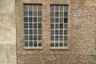 Two large industrial windows with small panes and metal bars are set in an old brick wall, showing