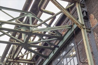 Metal framework supporting pipelines on an old brick wall in an industrial environment