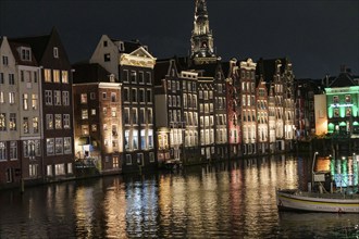 Row of houses on the canal with illuminated facades reflected in the water, Amsterdam, Netherlands