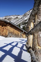 Snow-covered mountain hut with wood in a sunny winter landscape, Neukirchen am Großvenediger,