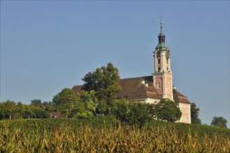 Baroque church stands majestically in the midst of a green landscape under a clear blue sky,