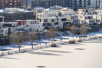 Residential buildings and pedestrians at the snow-covered and frozen Phoenix Lake in Dortmund,