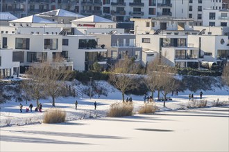 Residential buildings and pedestrians at the snow-covered and frozen Phoenix Lake in Dortmund,