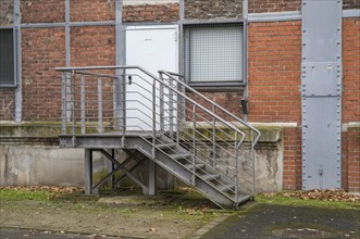 Metal staircase leading to a white door and barred window of a brick industrial building