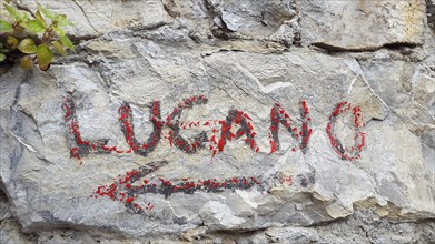 Hand painted red sign on a rock indicating the direction to Lugano, Switzerland, on Sentiero delle