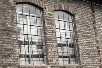 Close-up of two arched industrial windows with metal grids reflecting an empty white room in an old