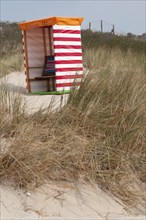 A red and white striped beach chair in front of sandy dunes and grasses, Borkum, l North Sea,