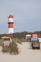 A lighthouse towers over a beach with several beach chairs and dunes, Borkum, l North Sea, GERMANY