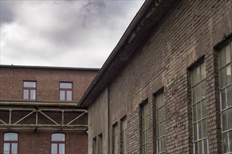 Exterior of an old decaying brick industrial building with metal pipe and cloudy sky