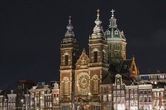 Illuminated church with striking towers and neighbouring buildings at night, Amsterdam, Netherlands