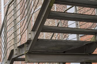 Metal fire escape with caged mesh wire alongside red brick building provides emergency exit route