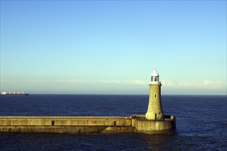 Lighthouse on a clear day with blue sky and sea, in the background a ship, Tynemouth, England,