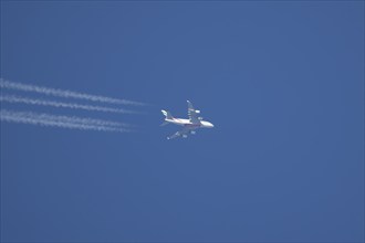 Airbus A380 aircraft of Emirates airlines flying across a blue sky leaving a contrail or vapor