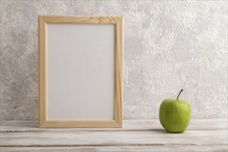 White wooden frame mockup with green apple on gray concrete background. Blank, vertical