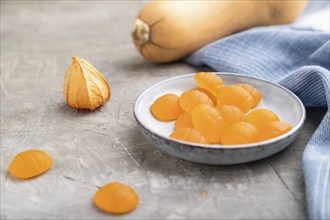 Jelly pumpkin candies on gray concrete background and blue linen textile. close up, side view,