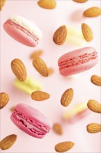 Multicolored flying macaroons and almonds frozen in the air on blurred pink background. top view,