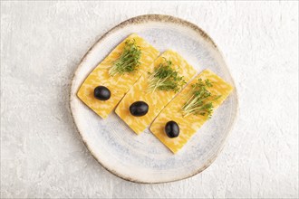 Marble cheese with olives and watercress microgreen on gray concrete background. top view, flat