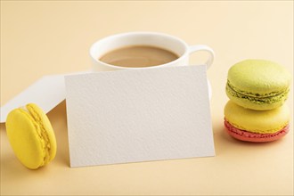 White paper business card mockup with yellow and green macaroons and cup of coffee on orange pastel