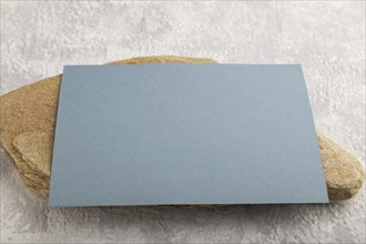 Blue paper business card, mockup with natural stone on gray concrete background. Blank, side view,