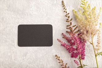 Black paper business card mockup with purple astilbe flowers on gray concrete background. Blank,