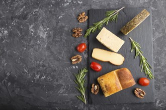 Smoked cheese and various types of cheese with rosemary and tomatoes on black slate board on a