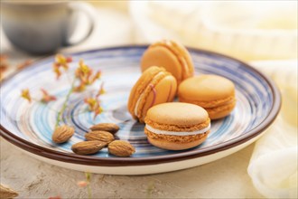 Orange macarons or macaroons cakes with cup of coffee on a white concrete background and linen