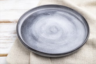 Empty gray ceramic plate on white wooden background and linen textile. Side view, close up