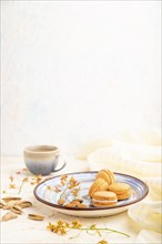 Orange macarons or macaroons cakes with cup of coffee on a white concrete background and linen