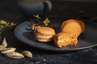 Orange macarons or macaroons cakes with cup of coffee on a black concrete background. Hard light,