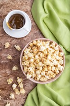 Popcorn with caramel in ceramic bowl on brown concrete background and green textile. Top view, flat