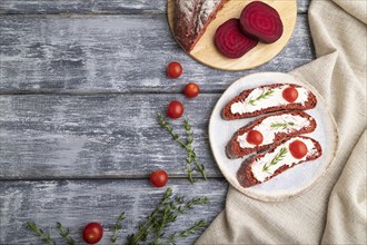 Red beet bread sandwiches with cream cheese and tomatoes on gray wooden background and linen