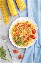 Corn noodles with tomato sauce and arugula on a gray concrete background and blue textile. Top