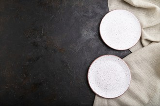 Two empty white plates on black concrete background and linen textile. Top view, copy space, flat