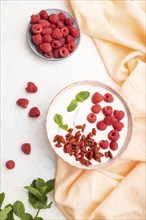 Yogurt with raspberry and goji berries in ceramic bowl on white concrete background and orange