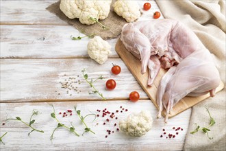 Whole raw rabbit with cauliflower, tomatoes and spices on a white wooden background and linen