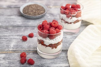 Yogurt with raspberry, goji berries and chia seeds in glass on gray wooden background and linen