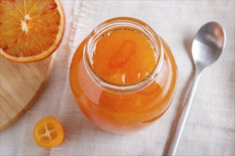 Orange and kumquat jam in a glass jar with fresh fruits on a white linen tablecloth. Homemade,