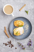 Cheese pancakes on a blue ceramic plate and a cup of coffee on a gray concrete background. top