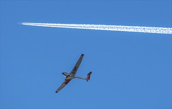 Twin-engine jet, passenger aircraft, with contrails, in the sky, below a motorised sailplane