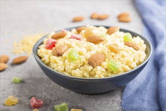 Millet porridge with candied fruits and almonds in blue ceramic bowl on a gray concrete background