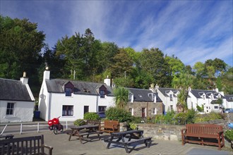 Small row of houses next to a square with benches, surrounded by trees under a blue sky, autumn,