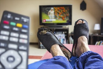 Remote control and couch potato, lazy man in comfy chair wearing worn slippers with big toes