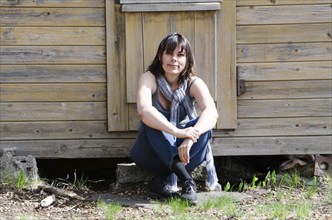 Woman Sitting Down in Front of a Entrance Door to a House and Waiting in a Sunny Summer Day in