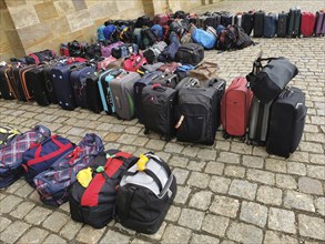 Luggage and rucksacks of different colours and sizes neatly lined up on a paved floor