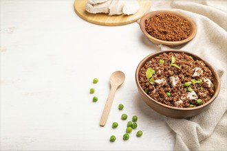 Quinoa porridge with green pea and chicken in wooden bowl on a white wooden background and linen